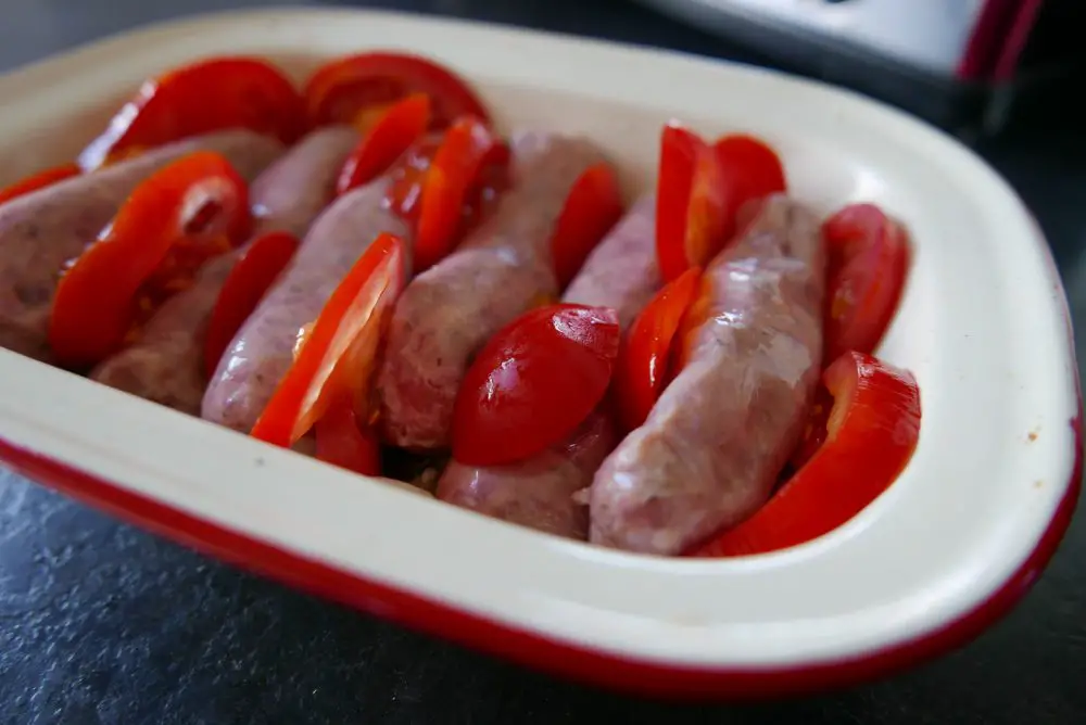 Making sausage pie with layers of sausages and tomatoes