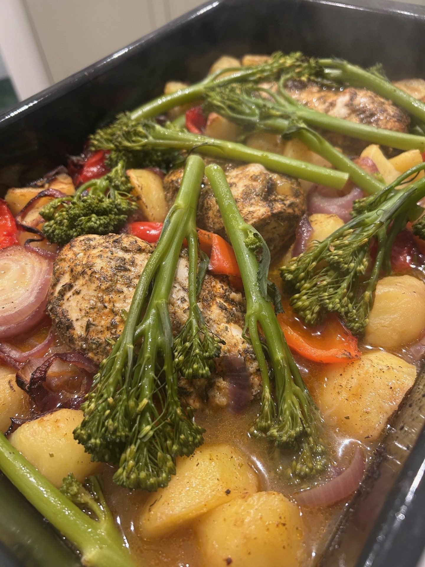 chicken tray bake just out the oven and ready for plating, with tender stem broccoli, red onion, peppers and potatoes