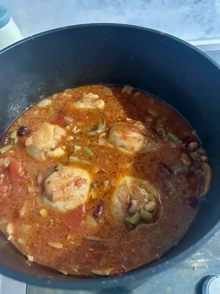 a cooking pot with chicken thighs bubbling in a tomato sauce