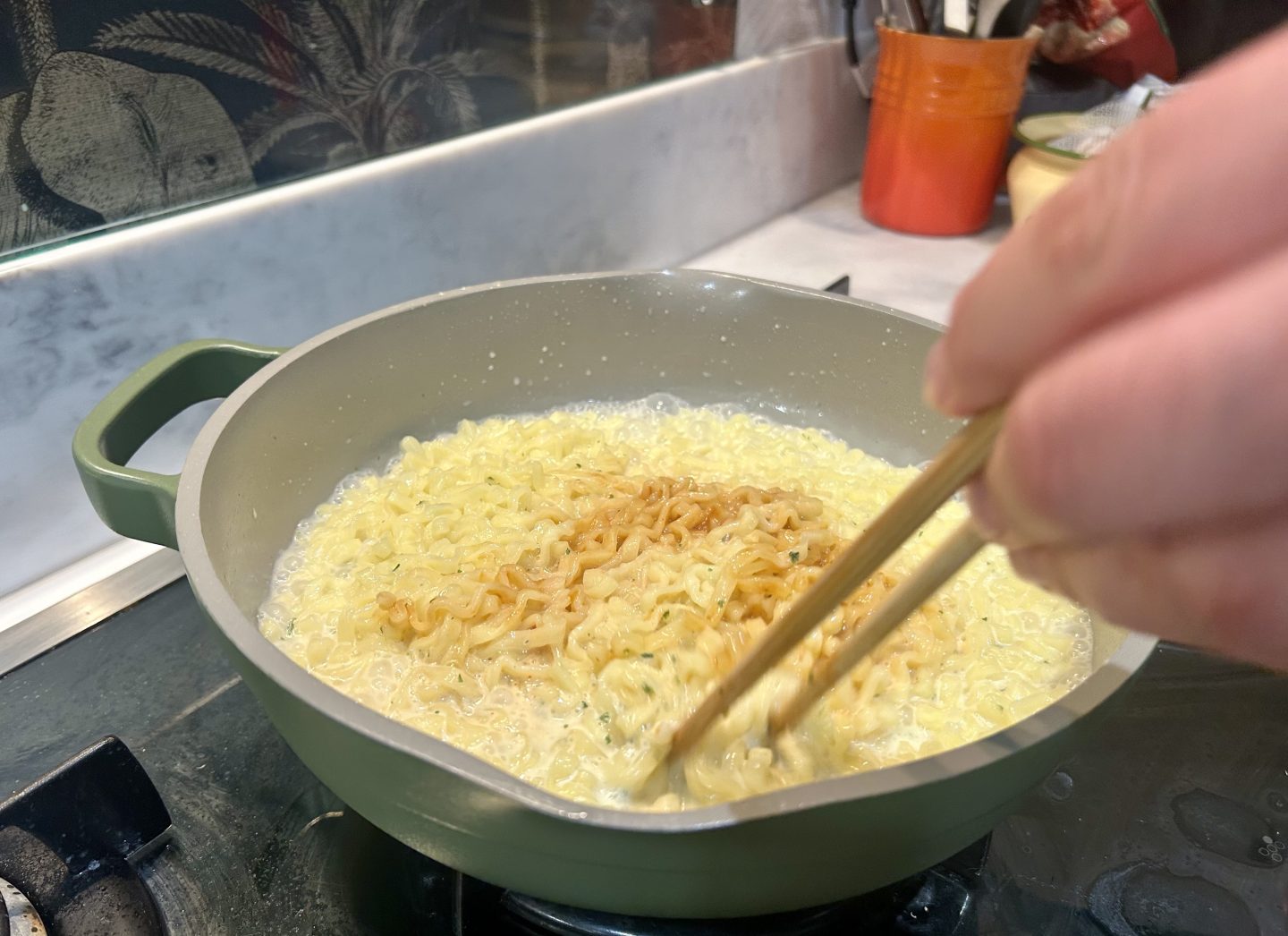 Stirring carbonara and spice sachets into boiling buldak noodles