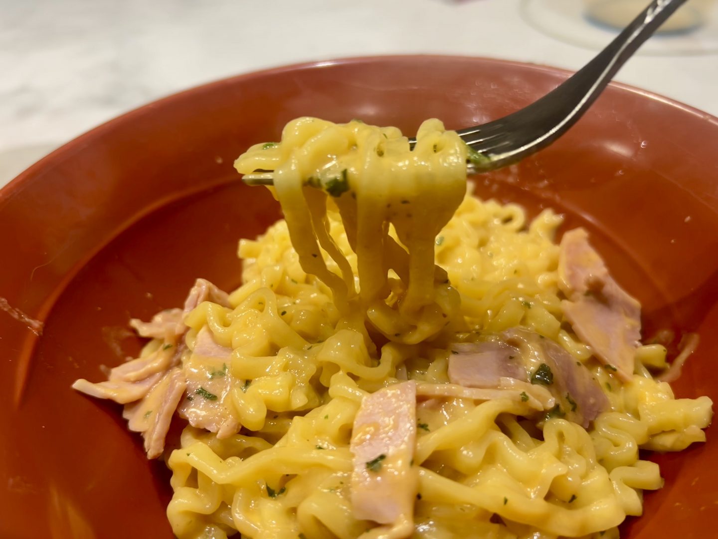 a fork full of creamy buldak noodles with added ham
