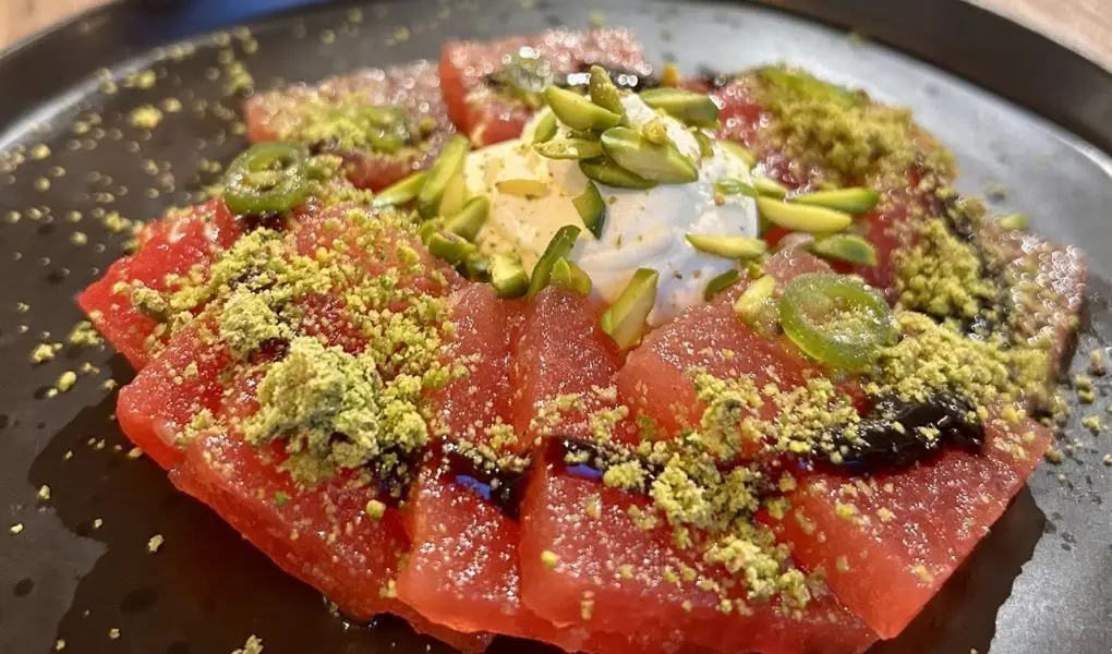 A plate of sliced watermelon, topped with whipped feta and crushed pistachio