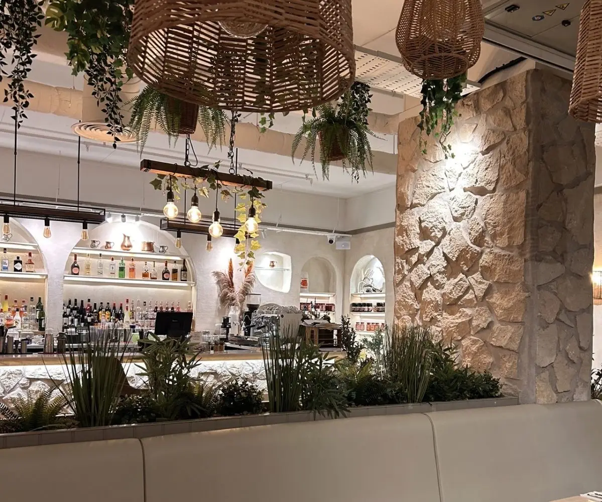A mediterranean looking restaurant with bright white lights, lots of plants and large wicker lampshades