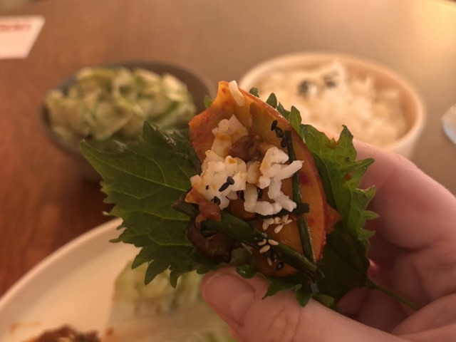 Korean ssam - a hand holding a perilla leaf with apple kimchi, pork, rice and chives.